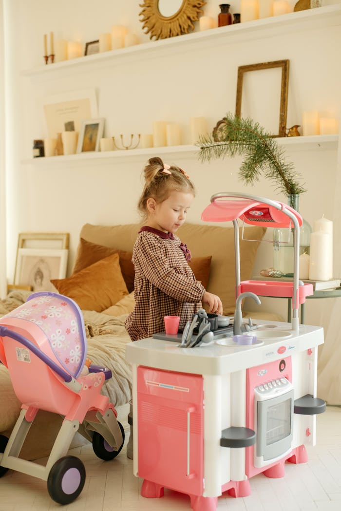 Category Young girl playing with a toy kitchen set in a cozy bedroom setting, expressing childhood fun.