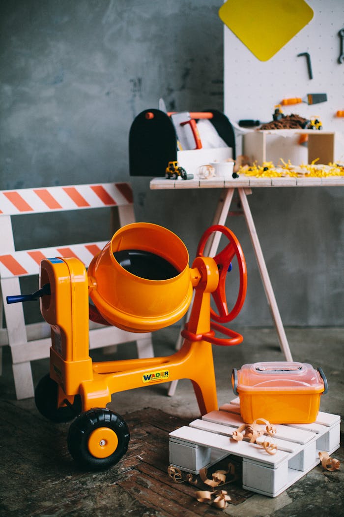 Category Colorful toy construction set featuring an orange cement mixer and tools.