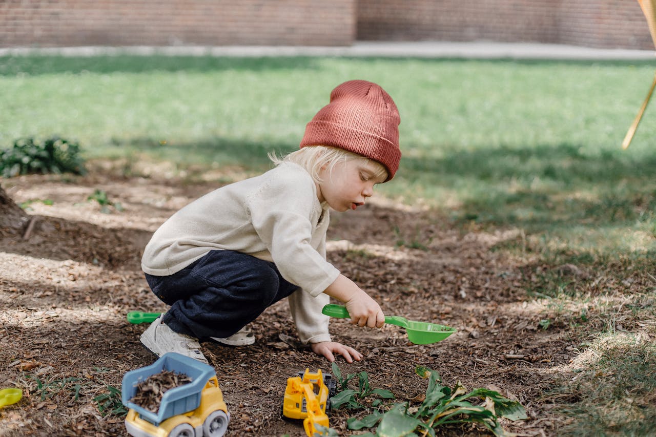 Home Side view of little boy in casual clothes and brown hat playing with plastic toys in backyard